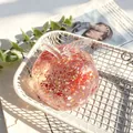 Rode glitter appel squeeze toy in een witte draadmand op een vintage krant achtergrond - Kerst Kerstman Vaseline Appel / Transparant Rood