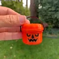 Nahaufnahme eines orangefarbenen Mini-Halloween-Kürbiseimers in der Hand gehalten. - Lachender Ausdruck / Orange C
