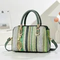 Detalle de bolso tipo almohada tejido a rayas verdes con colgante de hoja y toques dorados - Verde