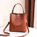 Elegant brown crocodile pattern bucket bag with adjustable crossbody strap and top handle. - Earthy Yellow