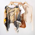 Détail d'un élégant poncho en soie satinée imprimée sur un cintre en bois naturel - Hauts / Floral Noir Jaune Orange (TS2402)