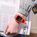 Red square LED digital watch for kids worn on wrist with magazine scene background. - Red