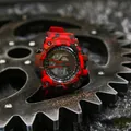 Detailed view of a red camouflage digital sports watch resting on a heavy metal gear. - Camouflage Red