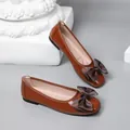 Close-up detail of brown patent leather ballet flats featuring an elegant satin bow - Tan