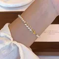 Détail d'un élégant bracelet de perles avec un charme de feuille dorée sur le poignet - Style Épi de Blé Perle (MY36425)