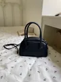 Black textured pillow bag with top handles and shoulder strap in a cozy bedroom setting. - Black