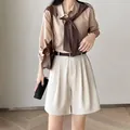 Styling view of high-waisted cream pleated shorts with a dark belt and beige blouse - S / Bottoms / Off White