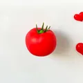 Close-up of realistic artificial tomato fridge magnet on white surface - Tomato