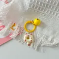 Close-up of a cute cartoon cat donut keychain with a yellow bell on white fringe. - Brown Cat + Yellow Ring + Yellow Bell