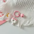 Close-up of a cute pink and white cat donut keychain charm resting on a white textured fabric - White Pink Cat + Pink Ring + Pink Bell