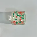 Makroaufnahme von quadratischem Weihnachts-Stressabbau-Spielzeug mit roten und grünen Elementen - Mittel / Mehrfarbig