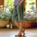 Side view of women's loose olive green cotton linen shorts with pockets in garden setting. - S / Bottoms / Army Green