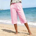 Detailed view of pink checkered capri pants worn by a model on a sunny tropical beach - S / Bottoms / Pink