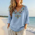 Detailed view of boho V-neck cotton linen blouse with colorful embroidery on a beach - Light Blue