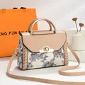 Detalle de un bolso de mano beige estampado con asas doradas y diseño floral paisley. - 23x11x18cm / Caqui