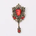 Close-up detail of a vintage palace style brooch featuring red gems and green crystals. - Red