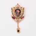 Detailed view of vintage court brooch with wine red crystal and gold hollow-out metalwork - Purple