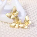 Set of three elegant matte gold butterfly brooches displayed on a white jewelry stand - Gold