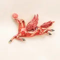 Vintage Pegasus brooch with red crystals and rose detail on textured fabric background. - Red