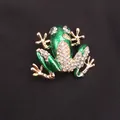Vista dettagliata di un'elegante spilla a forma di rana con strass verdi su tessuto nero - Rana in Smalto Verde con Strass Bianchi (a2-1-7002)