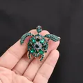 Dettaglio di una scintillante spilla a forma di tartaruga marina con cristalli verdi - Oro + Blu Pavone/Verde