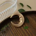 Close-up of vintage matte gold crescent moon brooch with a face design on a wooden tray - Moon Face Style
