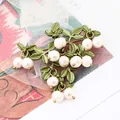 Vintage green cranberry leaf brooch detail featuring elegant white pearls on metal sprig design - White