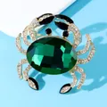 Detailed view of a gold crab brooch with a large emerald green crystal and pavé rhinestones. - Green