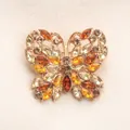 Elegante broche de mariposa con cristales ámbar y amarillos en fondo texturizado. - Amarillo