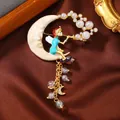 Vintage enamel brooch featuring a fairy sitting on a crescent moon with pearl dangles. - Moon Fairy Tassel Style (10)