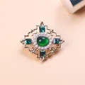 Macro view of detailed vintage Baroque brooch with green gemstone and white pearl accents - Turquoise Cross Style