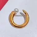 Close-up of elegant gold C-shaped brooch with a glossy white pearl accent - Gold