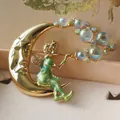 Détail macro d'une broche vintage lune dorée et fée verte avec des bulles irisées - Fée Soufflant des Bulles (Style 12)