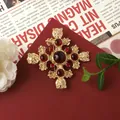 Detailed view of a vintage Baroque gold-tone brooch with red gems and lion heads. - Baroque Cross