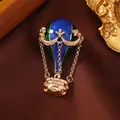 Macro detail of a creative enamel hot air balloon brooch featuring vintage gold chains - Hot Air Balloon / Blue