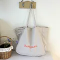 Vista detallada de un bolso tote grande de lona beige minimalista con letras naranja - Gris claro