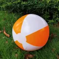 Close-up detail of an orange and white striped inflatable beach ball on green grass - Orange and White