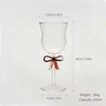 Elegant clear glass wine goblet featuring a decorative red bow tie on the slender stem - Red