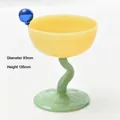 Close-up of yellow and green glass dessert bowl with wavy stem and blue bead. - Round Ball Stemware (bz2042) / Topaz and Jade