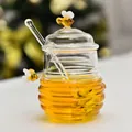Detail of a transparent glass honey jar with lid, glass stirrer, and bee accents. - Small Honey Jar with Two Bees