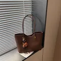 Vue détaillée d'un sac cabas en cuir marron avec des anses fines et un charmant pendentif. - Avec Pendentif / Café