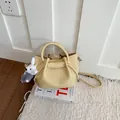 Elegant light yellow pebbled leather bucket bag featuring a cute white rabbit plush charm - Yellow With Pendant