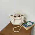 Chic off-white textured leather bucket bag with top handles on a wooden table. - White