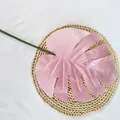 Gros plan d'une feuille de monstera artificielle rose avec tige verte sur tapis tressé. - Rose