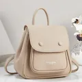 Close-up of beige pebbled leather backpack showing the front pocket and logo detail - Khaki