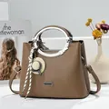 Close-up of a brown pebbled leather handbag with metallic handles and a decorative charm. - 23x11x18cm / Dark Khaki