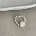 Macro detail of a minimalist elastic pearl ring featuring a unique carved floral centerpiece bead - Pearl Flower