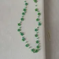 Gedetailleerd overzicht van handgemaakte groene kralen bloem ketting op beige textuur - Groen