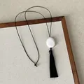 Detail of Zen style necklace with white pebble pendant and black tassel on canvas - White Resin Necklace