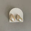 Detailed view of faceted champagne bean-shaped stud earrings on a textured display card - Irregular Bean Style / Cream